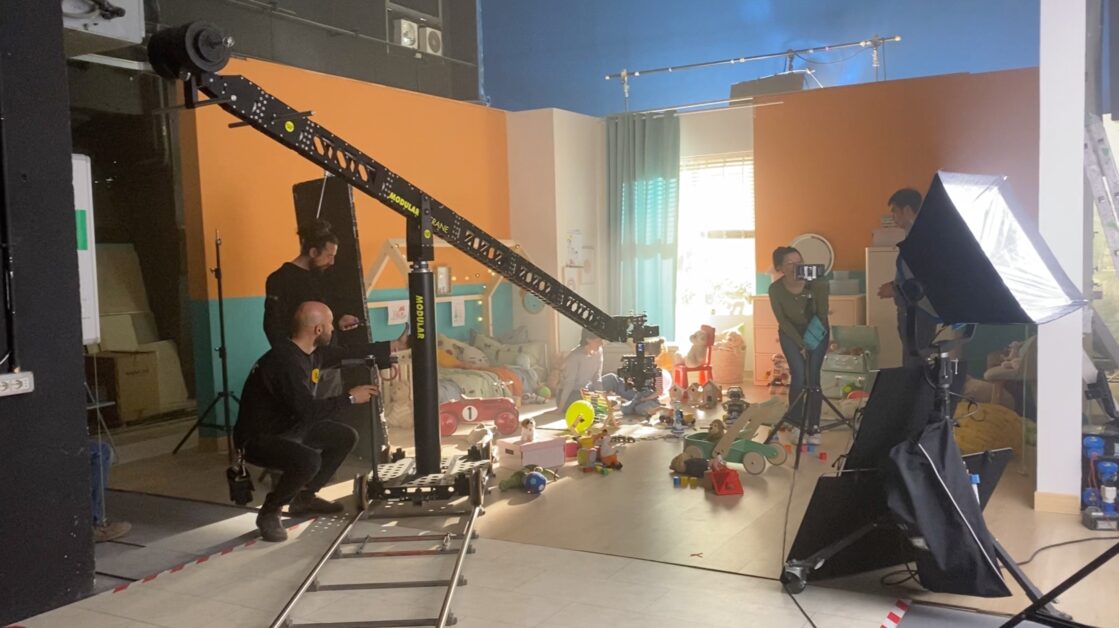Set cinematografico allestito in una cameretta colorata, con troupe e attrezzature professionali in azione
