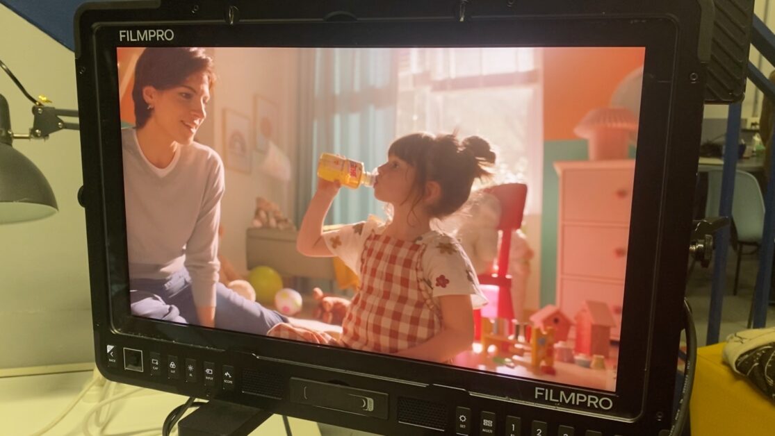 Monitor sul set mostra una bambina che beve Estathé mentre la madre le sorride in una stanza colorata