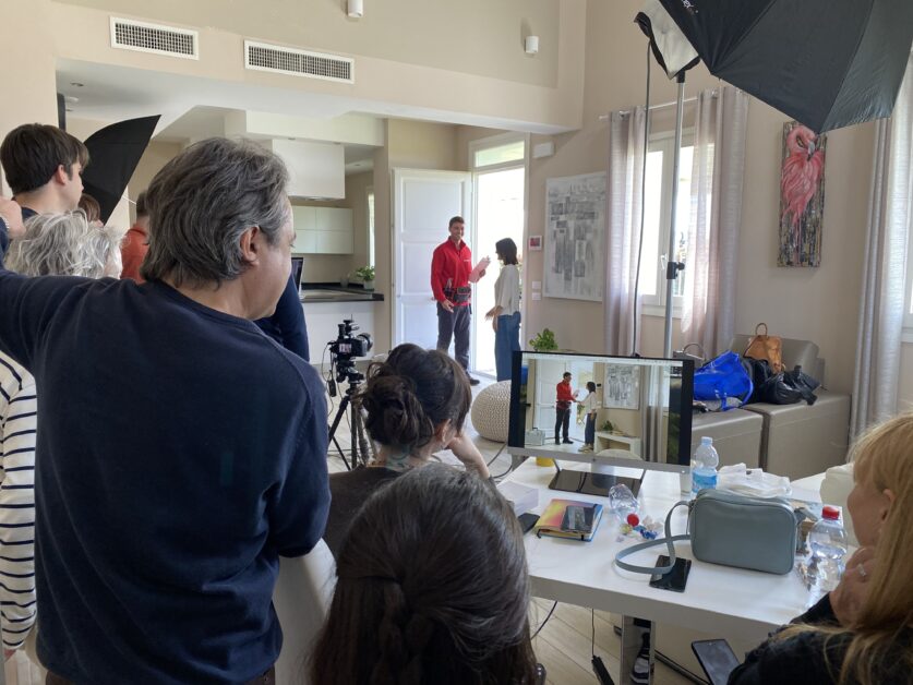 Backstage di uno spot Ariston con troupe al lavoro e monitor che mostra due attori durante una scena all’ingresso di una casa